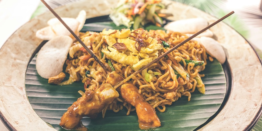 A mouth-watering view of a plate served with noodles and chopsticks with vegetables.