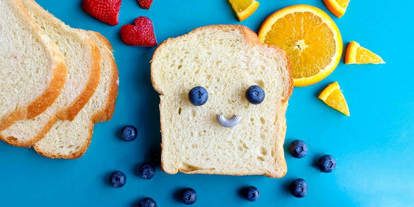 A view of a slice of bread with blueberries on top and slices of oranges on the side.