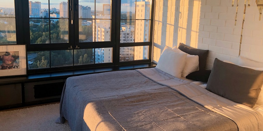 A view of a hotel room with a bed lined with grey and white sheets and two pillows on it.