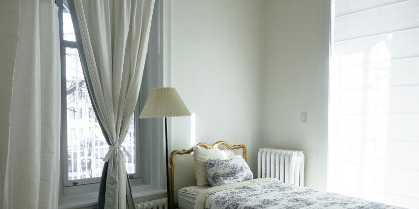 A view of a room with a bed lined with white and blue floral comforters and a lamp.