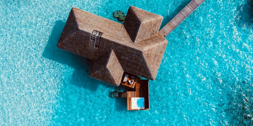 A breathtaking view of a villa with a brown roof surrounded by turquoise waters on all sides