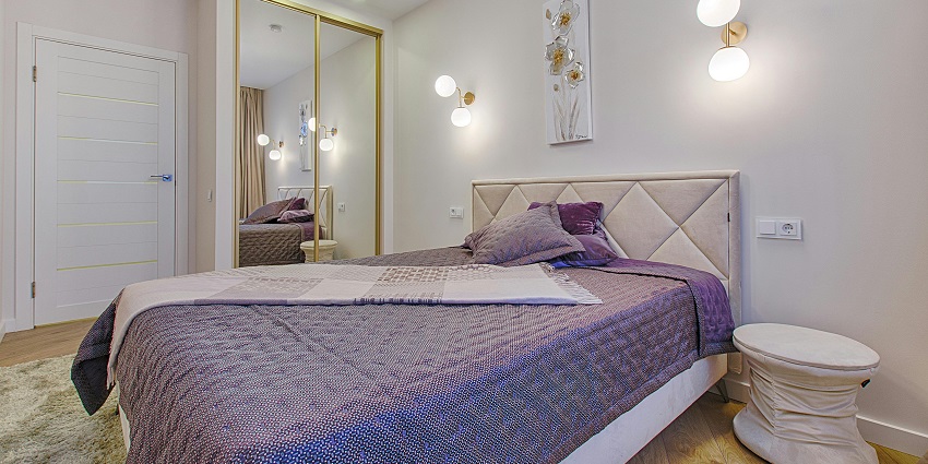 A view of a room with a bed lined with grey and white sheets with a mirror on the side.