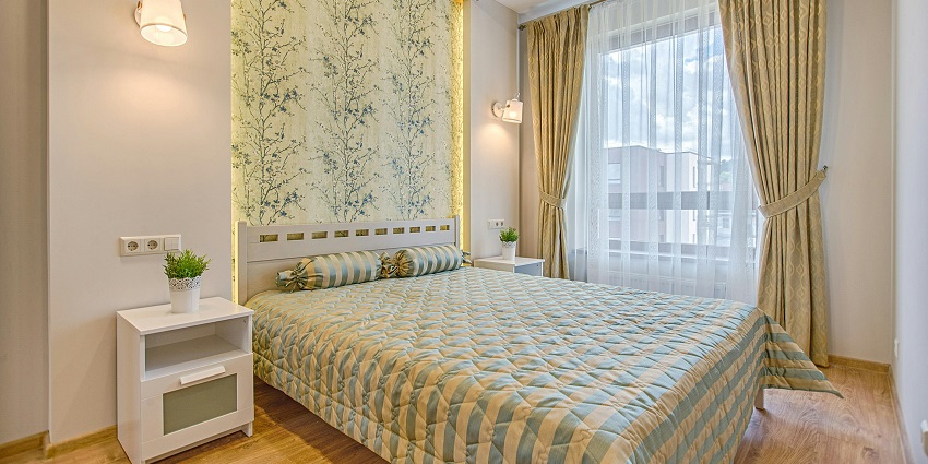 A fascinating view of a room with a bed lined with colourful sheets and open curtains.