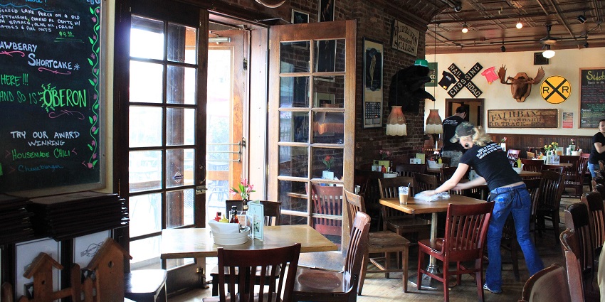 A whiskey bar with a table chair setting inside being cleaned by a person