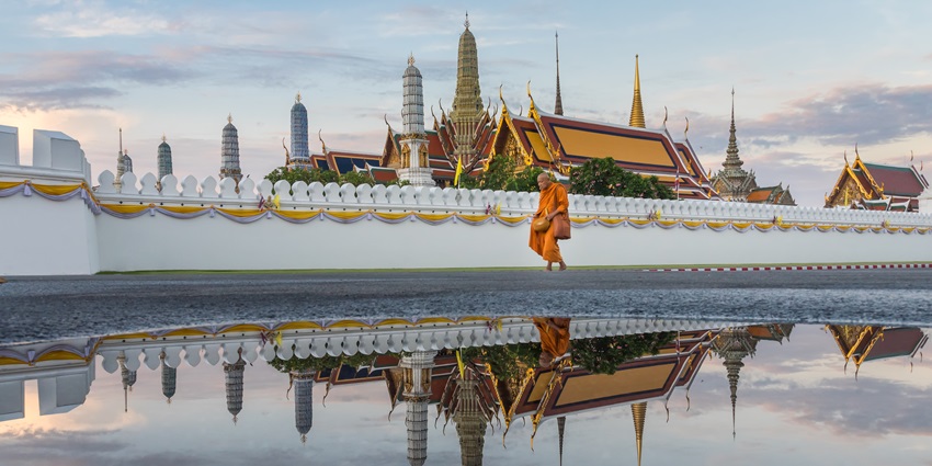 A monk walks in the morning after the rain in front of the Temple of the Emerald Buddha