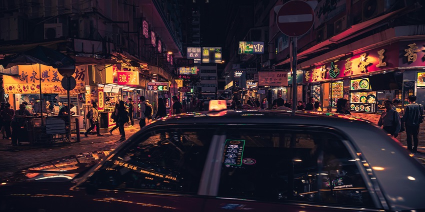 Taxi driving near high-rise buildings during nighttime with city lights reflecting.