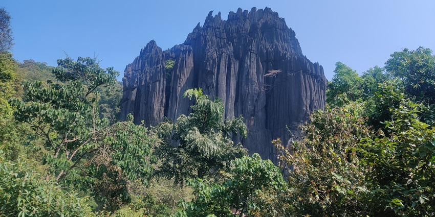 A frontal view of a majestic cave system near Apsarakonda Waterfalls, surrounded by green hills