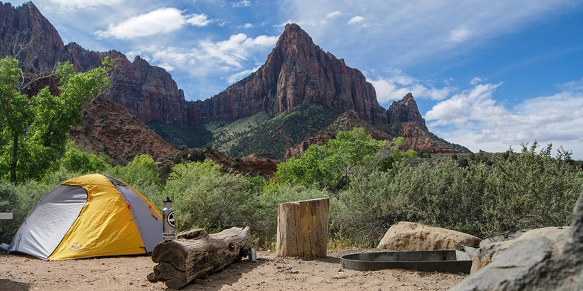 view of yellow and grey dome tent near tree stump with rocky mountain under cloudy sky.