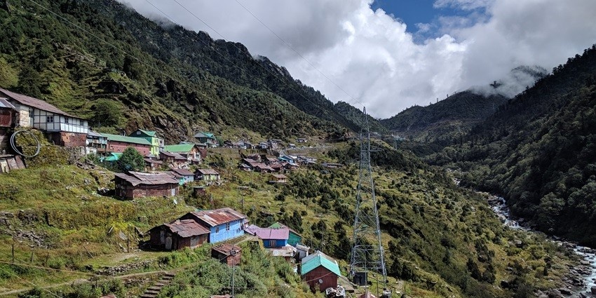 A view of Yuksom Valley decked with lush greenery, giant peaks, and colourful houses.