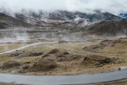 A view of a majestic mountain range with a narrow strip of road in between under clouds.