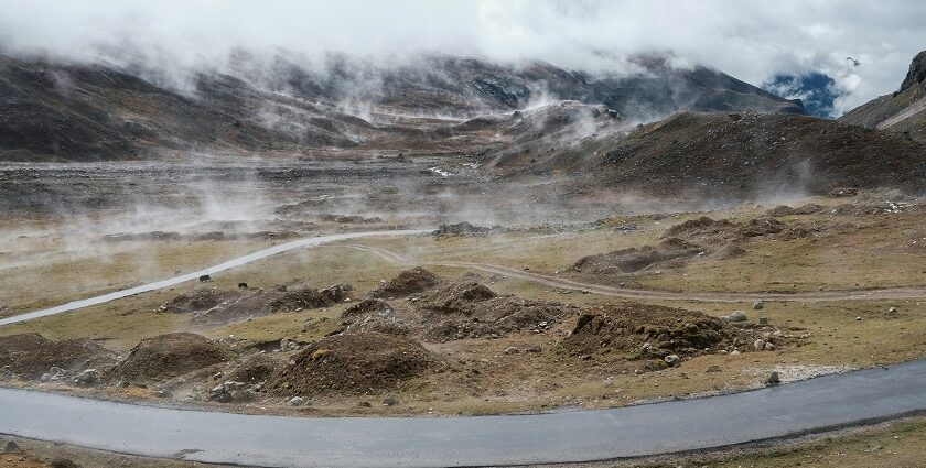 A view of a majestic mountain range with a narrow strip of road in between under clouds.