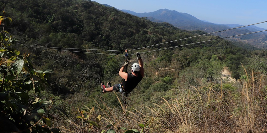 A view of a person gliding through a cable amidst the lush green vegetation and peaks.