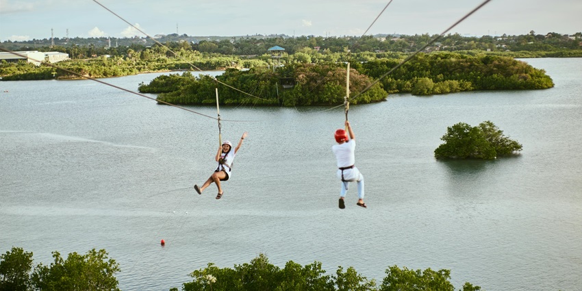 A couple enjoying ziplining over clear water view and lush greenery surrounded
