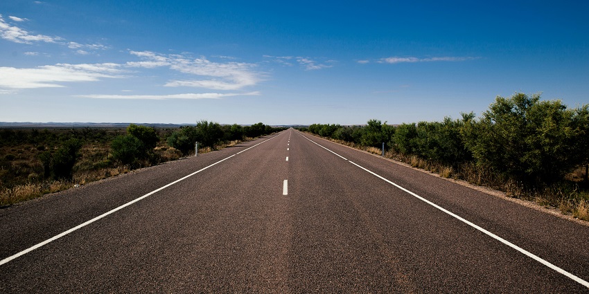 A stunning view of a gray road surrounded by lush green trees during the daytime.