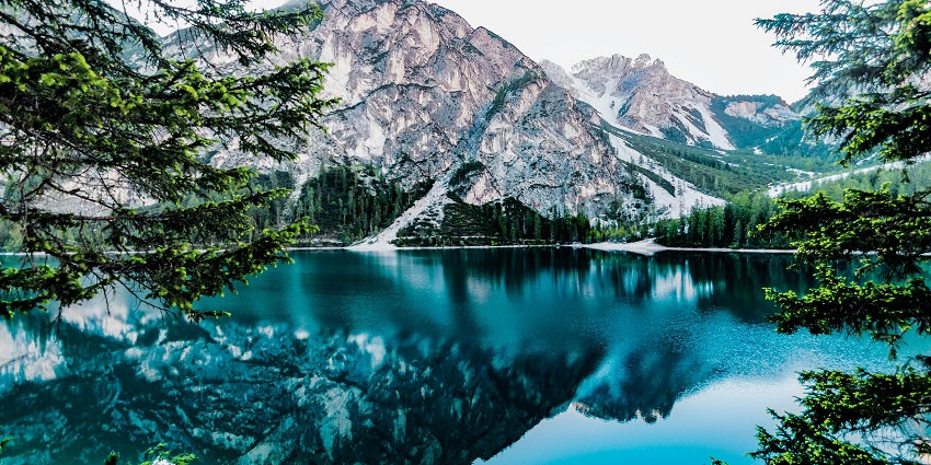 Serene lake reflecting mountains under a bright white sky, creating a peaceful scene.