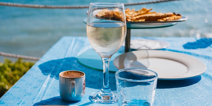 A tempting view of a drink glass on a table with a sparkling water body in the backdrop.