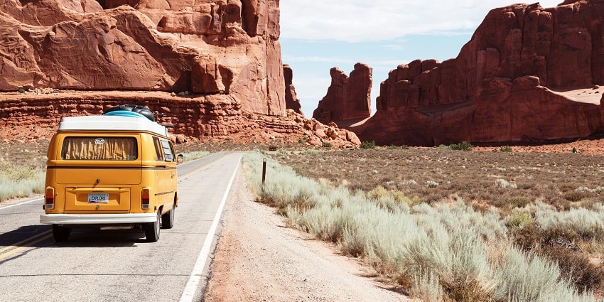 A cheerful yellow Volkswagen van driving along a scenic road surrounded by greenery.