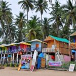 A view of a row of shacks along the shoreline of a beach in Goa with the backdrop of trees