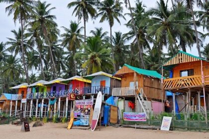 A view of a row of shacks along the shoreline of a beach in Goa with the backdrop of trees