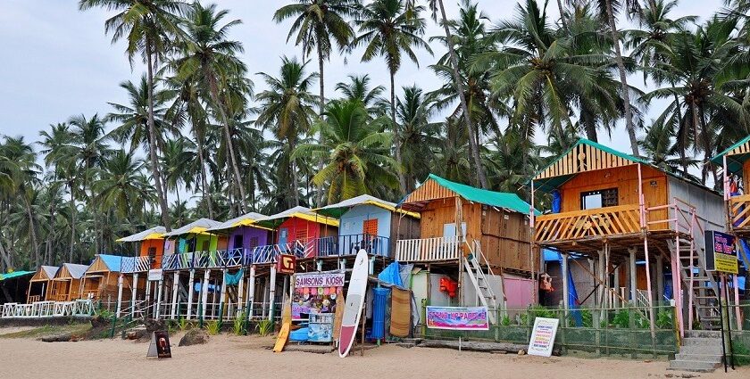 A view of a row of shacks along the shoreline of a beach in Goa with the backdrop of trees