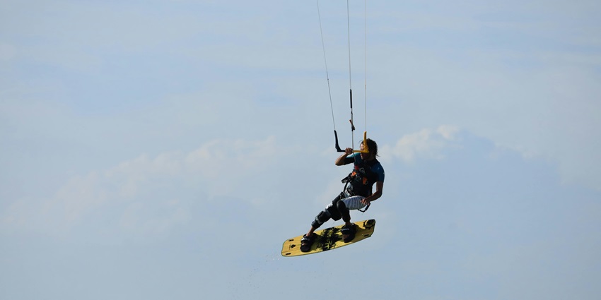 Kiteboarder jumping above waves against a clear blue sky