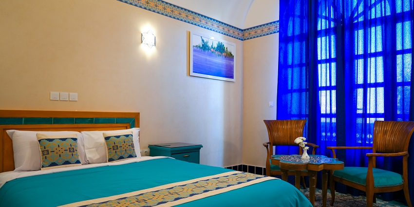 Image of cosy bedroom featuring a bed, chair, and a beautiful painting on the wall.