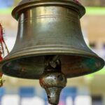 Close-up of a brass bell mounted on a wooden pole against a clear blue sky.