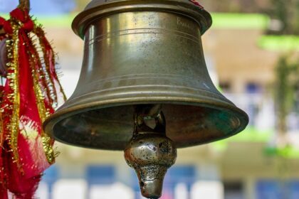 Close-up of a brass bell mounted on a wooden pole against a clear blue sky.