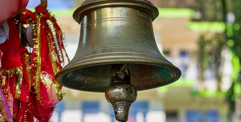 Close-up of a brass bell mounted on a wooden pole against a clear blue sky.