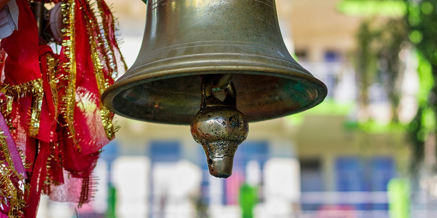 Temple bell hanging on a pole, with intricate details and a clear view of the clapper.