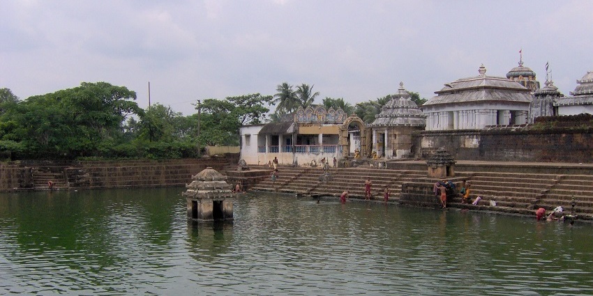A breathtaking view of a holy pond in front of a temple with multiple people taking a dip.