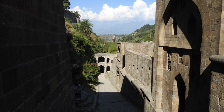 A large fort with sunny shadows being cast on its exterior in the peaks of the Himalayas.