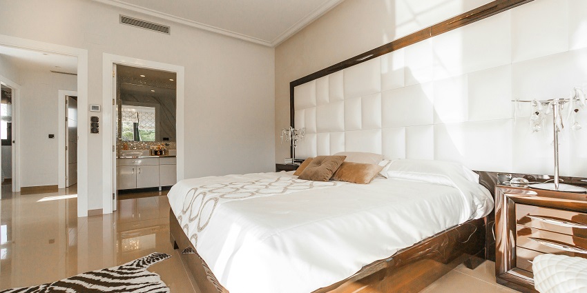Brown wooden bed frame with white cover, beside a matching wooden nightstand in a softly lit room.