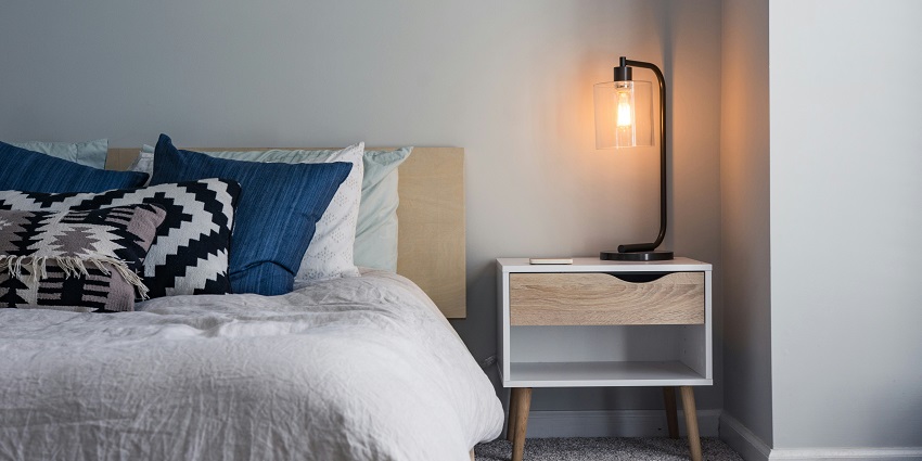Image of black table lamp on a nightstand, casting a warm glow in a dimly lit room.