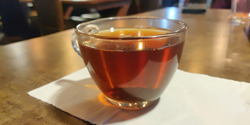 Traditional hot black tea from Kerala served in a glass cup on a wooden table in a cafe.