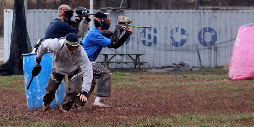 A group of friends playing paint ball, hiding behind the drums and firing