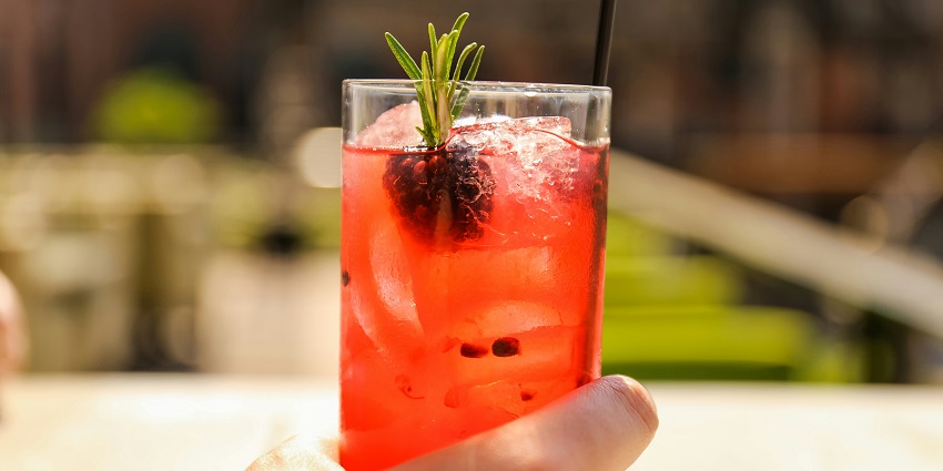 A filled glass of red drink and a person holding it, capturing the warm ambiance