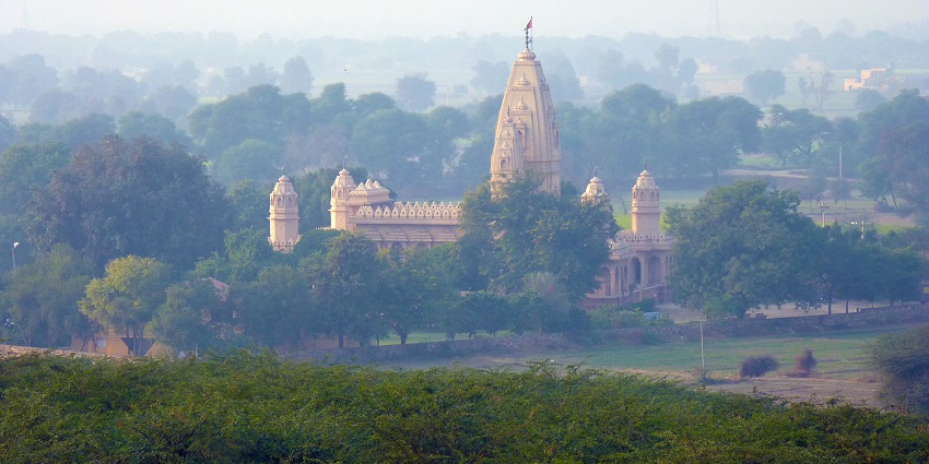 A picture of a temple in Hisar taken from a distance with a green hill visible