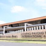 a frontal view of an airport with yellow architecture and bold letters during the daytime.