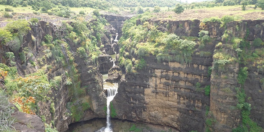 A view of the majestic waterfalls at the Ajanta Caves in Maharashtra, surrounded by trees and greenery