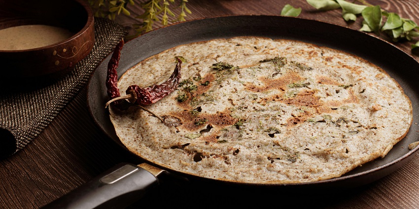 A close-up view of an appetising aloo paratha in a frying pan served with red chillies.