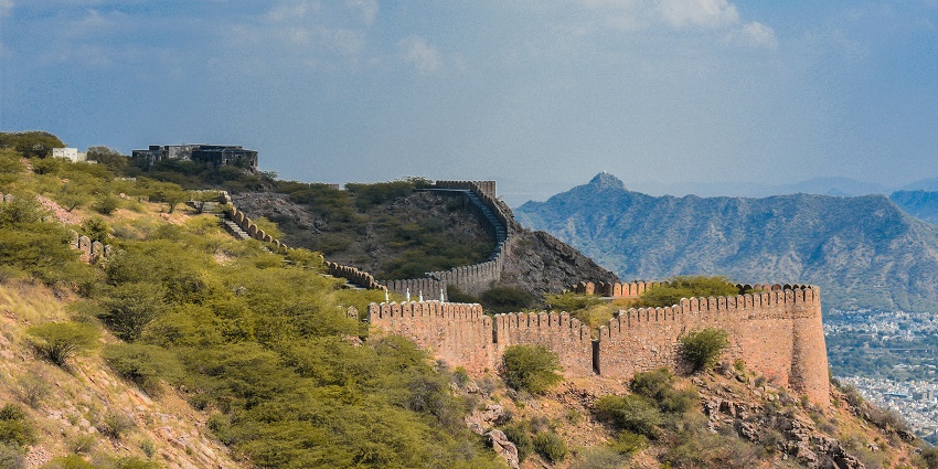 An aerial view of Alwar Fort in Rajasthan surrounded by green-capped peaks and mist.