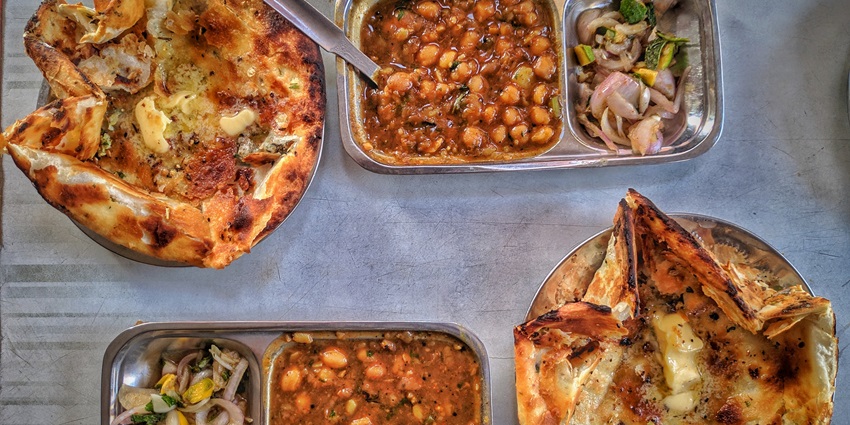 A mouth-watering view of a plate served with delicious cooked curries with a flatbread.