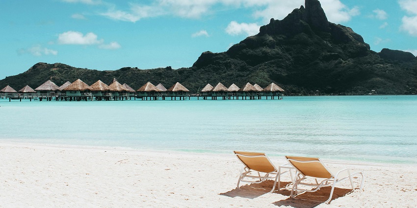 Serene island scene featuring cosy cottages and beach chairs by the tranquil water.
