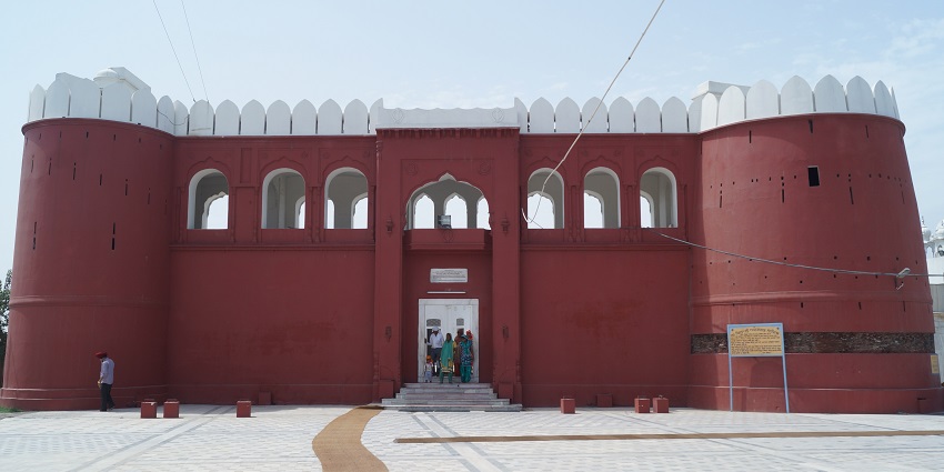 A picture of a gurudwara fort taken from the front with its tall red walls visible