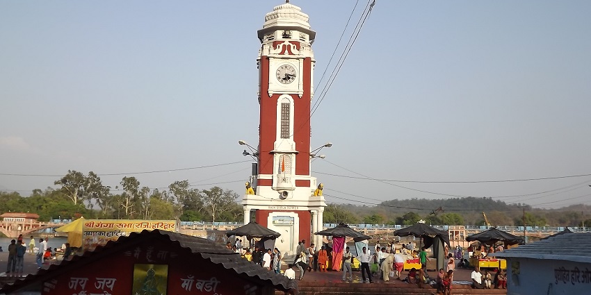 A distant picture of a clock tower in the middle of a street with traffic moving around