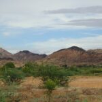 A picture of a couple of hills taken from a distance with green valleys surrounding the hills