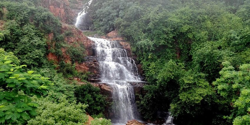 A famous waterfall in Visakhapatnam cascading down a hill surrounded by greenery