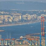 An aerial picture of a large water body with a city in the background with a sea port in front