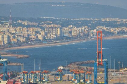 An aerial picture of a large water body with a city in the background with a sea port in front